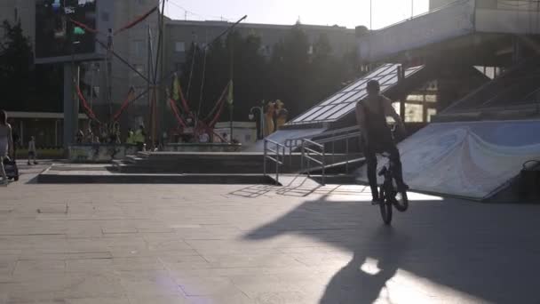 Atlético joven con una camiseta haciendo trucos de acrobacias en una plaza de la ciudad al atardecer . — Vídeos de Stock