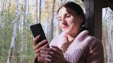 Mutlu çekici kadın, sonbahar bahar ormanlarında, sosyal ağlar üzerinden telefonla iletişim kuruyor.