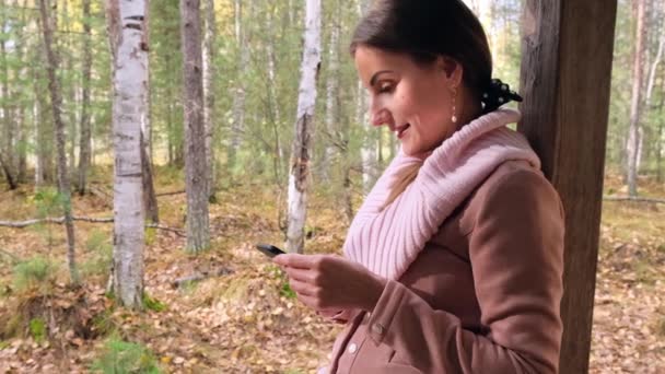 Šťastná atraktivní žena, v podzimním jarním lese, komunikuje na sociálních sítích po telefonu — Stock video