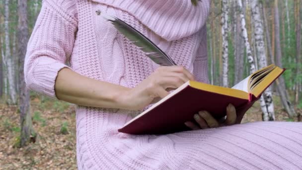 Happy attractive smiling woman writes poetry with feather in spring forest. — Stock Video