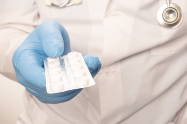 Beyaz elbiseli doktor ve boynunda steteskop olan mavi eldivenler hap tutuyor. Yakın çekim