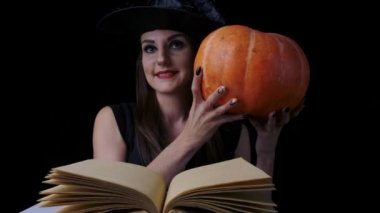 Açık bir büyü kitabı önünde siyah bir arka plan üzerinde Çekici cadı, bir kabak arkasından peeks ve onun ruh hali değişiklikleri her zaman gülümsüyor, cadılar bayramı kavramı.