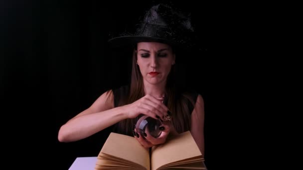 Привлекательная ведьма на черном фоне, держа свечу в руках над книгой заклинаний — стоковое видео