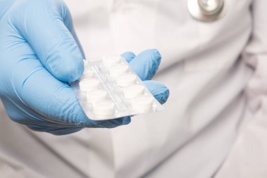 Beyaz elbiseli doktor ve boynunda steteskop olan mavi eldivenler hap tutuyor. Yakın çekim