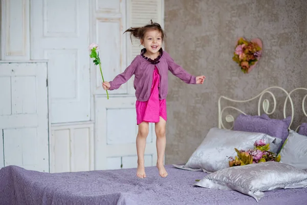 Kleines Mädchen Mit Blumen Springt Auf Dem Bett — Stockfoto