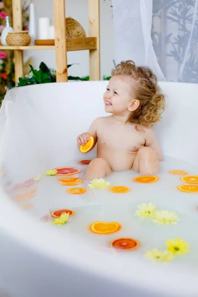 Child on the milk bath with flowersa little girl with curly hair in a milk bath with yellow flowers and orange oranges, red grapefruits.