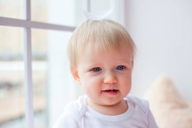 Küçük beyaz bir kız pencere kenarında tek başına oturuyor ve beyaz tüylerle oynuyor..