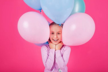 Renkli balonları olan güzel bir kız pembe arka plana gülüyor. Yüzüne balon yapıştırmış bir kızın büyük bir portresi. Pastel renkli bir balonla oynar ve kutlar.