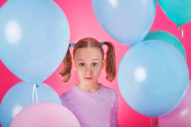 Renkli balonları olan güzel bir kız pembe arka planda gülüyor. Doğum günü partisindeki güzel mutlu genç kadın. Neşeli model eğleniyor, oynuyor ve pastel renkli balonla kutluyor.