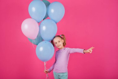 Renkli balonları olan güzel bir kız pembe arka planda gülüyor. Doğum günü partisindeki güzel mutlu genç kadın. Neşeli model eğleniyor, oynuyor ve pastel renkli balonla kutluyor.