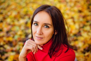 Kırmızı kazaklı bir kadın, sarı akçaağaç yapraklarının arasında bir battaniyenin üzerinde parkta oturuyor. Doğada sonbahar pikniği.