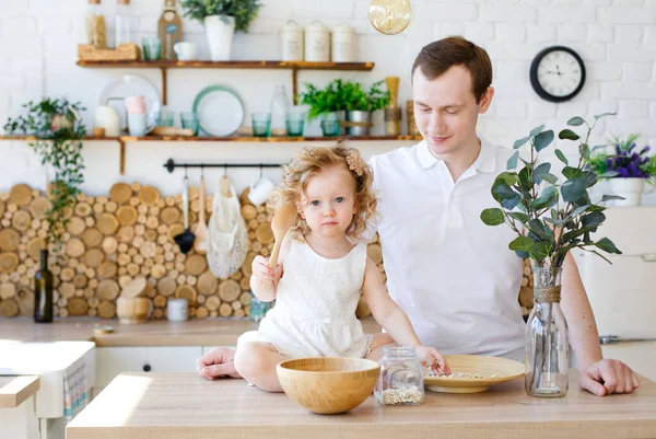 Caucasian dad and daughter, funny dad and girl hugging and cooking together in the kitchen in a bright kitchen, lifestyle and father\'s Day, single parents