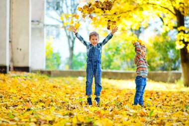 Çocuk parkta sarı sonbahar yapraklarıyla oynuyor.