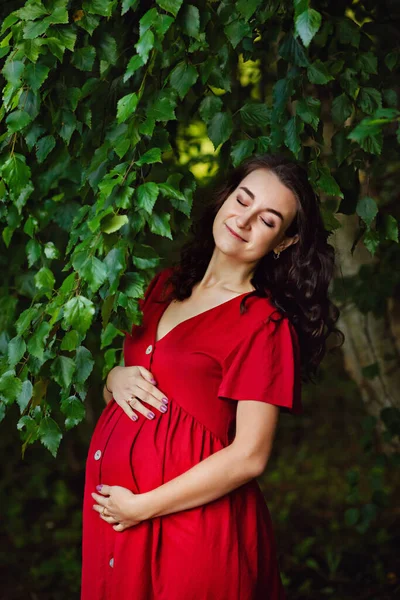 Elinde Çiçekleri Olan Kırmızı Elbiseli Mutlu Hamile Bir Kadın Dinleniyor — Stok fotoğraf