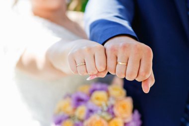 Gelinin ve damadın elleri. Gelin ve damat bir düğün töreninde el ele tutuşuyorlar. Yeni evlilerin elinde evlilik yüzükleri var. Yeni evlilerin elleri düğün çiçeğinin arka planında.