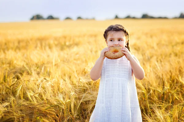 Beyaz bir elbise içinde gülümseyen küçük bir kız ve açık havada simit olan buğday tarlasında iki at kuyruğu. Bir simidi ısırıp koparır..