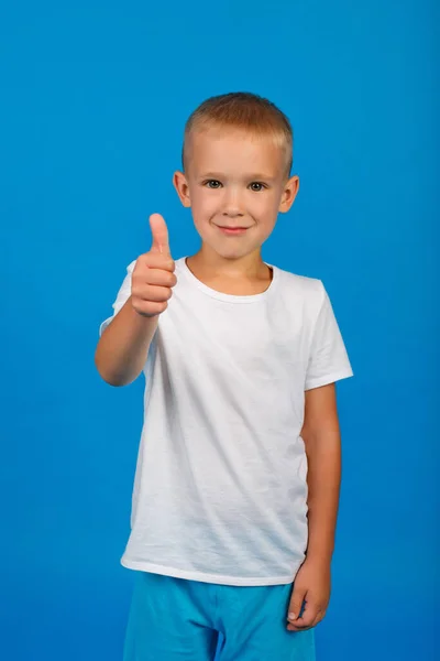 一个年轻的白种人 蓝眼睛 身穿蓝色背景的白色T恤 竖起大拇指 — 图库照片