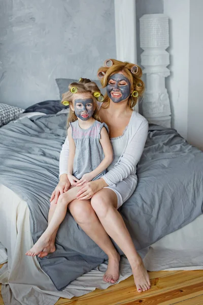 Mother and child do cosmetic procedures together. Happy family mother and little daughter make a face mask in the bedroom sitting on the bed.. Concept of a beauty salon, Spa and Wellness center.