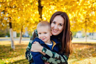 Genç ve güzel bir anne, genç oğluyla sonbahar parkında oynuyor..