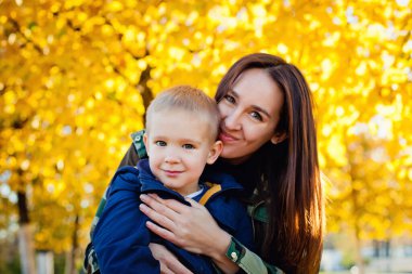 Genç ve güzel bir anne, genç oğluyla sonbahar parkında oynuyor..