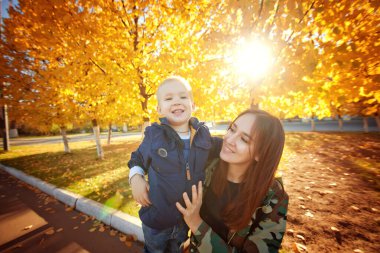 Güz Parkı 'nda bir bankta oturan güzel anne ve oğul. Açık hava fotoğrafları. Ebeveynler ve çocuklar arasındaki ilişkiler. Anneler Günü.