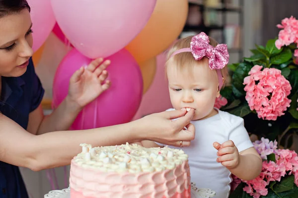 Aile masada, doğum günü pastası ve balonlarla. İlk senenin kutlaması. Bir anne kızına pasta yedirir..