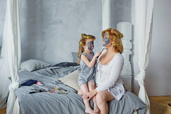 Mother and child do cosmetic procedures together. Happy family mother and little daughter make a face mask in the bedroom sitting on the bed.. Concept of a beauty salon, Spa and Wellness center.