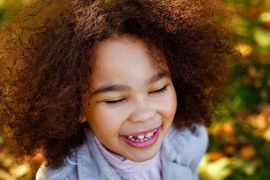 Şirin Afro kız açık havada gülümsüyor, piknik yapıyor ve parkta sonbahar gününün tadını çıkarıyor. Yapraklarla oynamak.