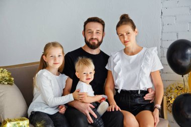 Mutlu bir anne ve babanın portresi kanepeye oturmuş, tatilde aile fotoğrafı çektirmek için poz veriyor. Kameraya bakarken küçük tatlı oğlana ve kızına sarıl.