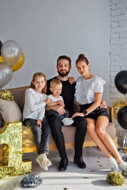 Mutlu bir anne ve babanın portresi kanepeye oturmuş, tatilde aile fotoğrafı çektirmek için poz veriyor. Kameraya bakarken küçük tatlı oğlana ve kızına sarıl.