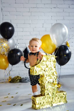 İlk doğum gününde, altın, siyah ve gümüş renkli bir partide tatlı sarışın çocuk. Altın numarayı tutuyor..