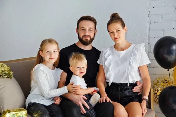 Mutlu bir anne ve babanın portresi kanepeye oturmuş, tatilde aile fotoğrafı çektirmek için poz veriyor. Kameraya bakarken küçük tatlı oğlana ve kızına sarıl.