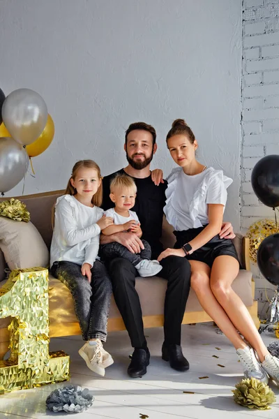 Mutlu bir anne ve babanın portresi kanepeye oturmuş, tatilde aile fotoğrafı çektirmek için poz veriyor. Kameraya bakarken küçük tatlı oğlana ve kızına sarıl.