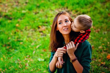Parktaki genç bir anne ve oğulun büyük portresi. Mutlu bir aile: bir anne ve çocuk sonbahar doğa yürüyüşünde kucaklaşarak oynuyorlar..