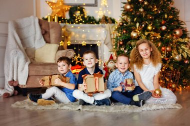 Evdeki Noel ağacının altında bir grup çocuk. Süslü kostümlü kızlar ve erkekler kış tatilini kutluyor. Çocuklar şöminenin yanındaki hediyeleri açın..