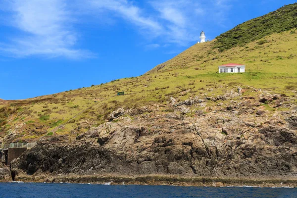 Cape Brett, New Zealand. The lighthouse on top of the cliff has been guiding mariners into the Bay of Islands since 1910. Beneath it is the old lighthouse keeper\'s house, now accommodation for hikers