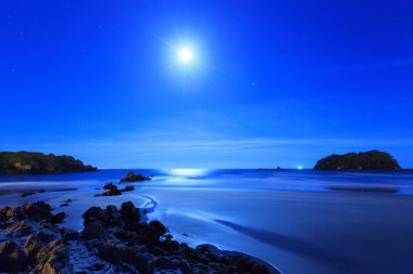 Dolunay plaj ve okyanus üzerinde gece, aydınlatıcı rock mostraları ve küçük deniz adalar parlar. Mount Maunganui beach, Yeni Zelanda
