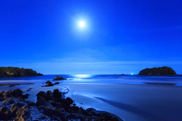 Dolunay plaj ve okyanus üzerinde gece, aydınlatıcı rock mostraları ve küçük deniz adalar parlar. Mount Maunganui beach, Yeni Zelanda