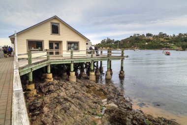 Oban, Stewart Adası, Yeni Zelanda. Rıhtımdan Halfmoon Körfezi manzarası. Ön planda bina, kazıklar tarafından desteklenen su üzerinde oturur