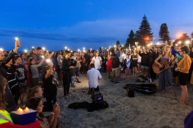 Mount Maunganui beach, Yeni Zelanda, 15 Mart kurbanları için bir alacakaranlık nöbeti Christchurch Camii çekimleri. Seyirciler onların cep telefonu meşaleler tutarken bir kadın şarkıcı gitar çalıyor. Fotoğraflandı 16 Mart 2019