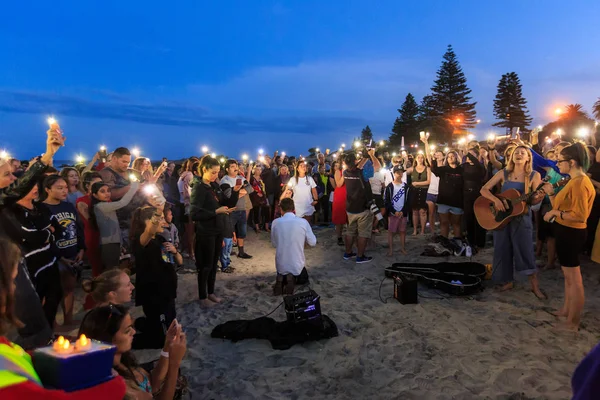 Mount Maunganui beach, Yeni Zelanda, 15 Mart kurbanları için bir alacakaranlık nöbeti Christchurch Camii çekimleri. Seyirciler onların cep telefonu meşaleler tutarken bir kadın şarkıcı gitar çalıyor. Fotoğraflandı 16 Mart 2019