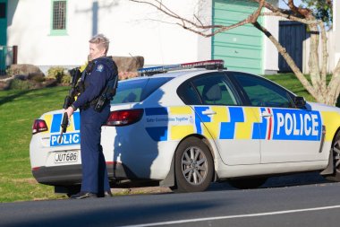 Yeni Zelanda Polisi'nin bir kadın üyesi, Bushmaster saldırı tüfeği ile silahlı, Tauranga bir polis arabası yanında duruyor, Yeni Zelanda, Haziran 22 2018