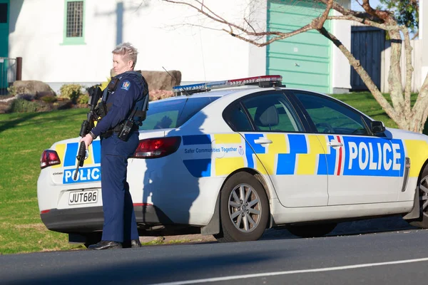 Yeni Zelanda Polisi'nin bir kadın üyesi, Bushmaster saldırı tüfeği ile silahlı, Tauranga bir polis arabası yanında duruyor, Yeni Zelanda, Haziran 22 2018