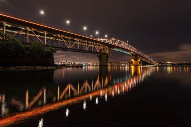 Auckland Harbour Köprüsü, Auckland, Yeni Zelanda, geceleri parlak bir turuncu yaktı. Köprünün kuzey ucundaki Stokes Point'ten şehrin ışıklarına bakarken görülüyor. 