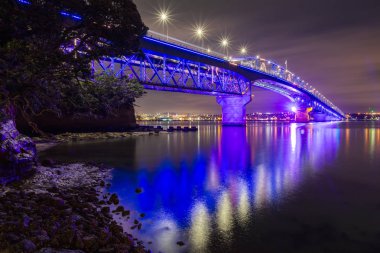 Auckland Harbour Bridge, Yeni Zelanda, renkli gece aydınlatması ile. Işık gösterisi Matariki kutlamak için, Maori Yeni Yıl. Bu manzara Stokes Point'ten güneye bakıyor. 