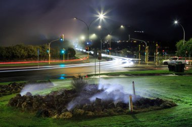 Rotorua, Yeni Zelanda, geceleri. Araba farları, jeotermal kaplıcalardan gelen buharı yol üzerinde dalgalı olarak yakıyor 
