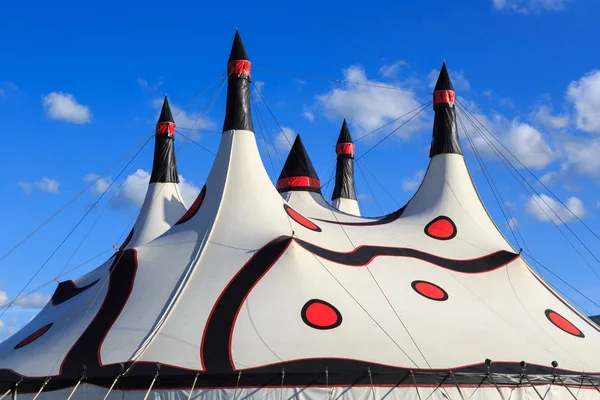 A big top circus tent, white with red dots and black swirl patterns, held up by many poles.
