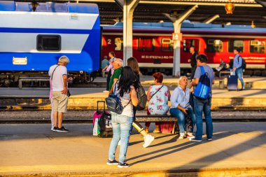 Tren bekleyen yolcular, platfor üzerinde bir bankta oturan