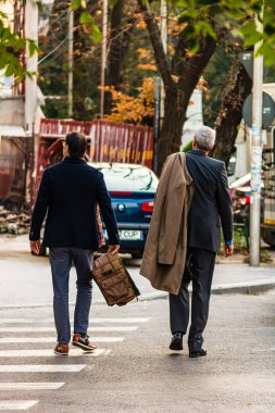 İki iş adamı caddeyi yaya geçidini kullanarak geçiyor.