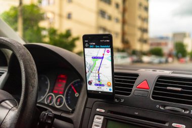 Araba gösterge panelindeki akıllı telefondaki waze haritaları uygulaması, sürücü, şehir trafiğinde doğru yolu göstermek için harita uygulaması kullanıyor. Bükreş, Romanya, 2020.